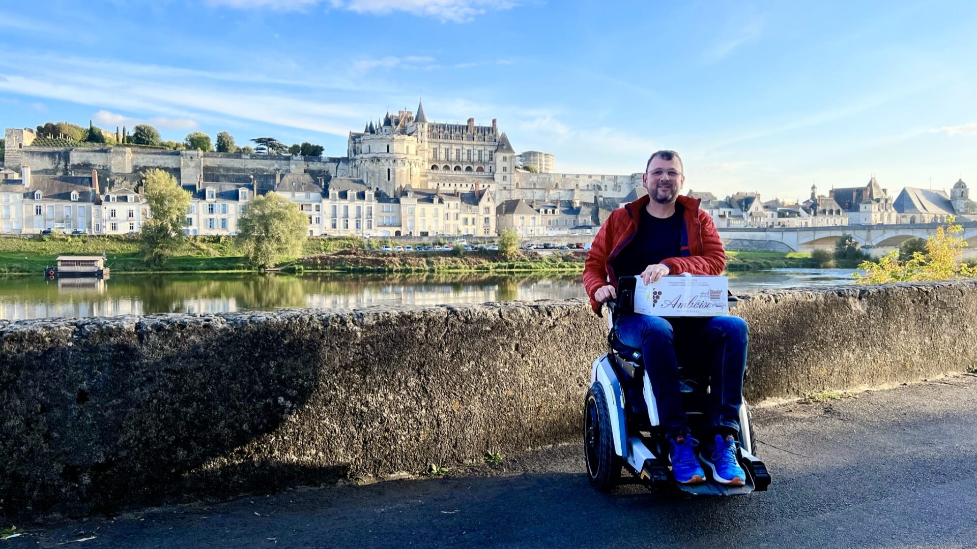 Un homme en fauteuil roulant électrique Scewo BRO avec le château d'Amboise en arrière-plan