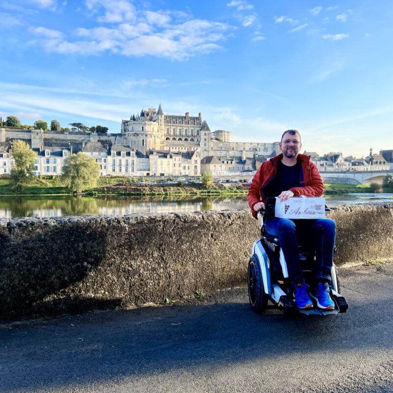 Un homme en fauteuil roulant électrique Scewo BRO avec le château d'Amboise en arrière-plan