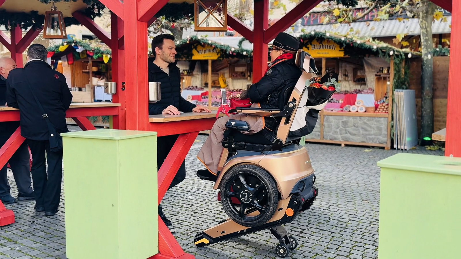 Höher sitzen, mehr erleben: Der Scewo BRO im Höhenverstellmodus ermöglicht Anne Teilhabe und Mobilität an einem Stand auf dem Weihnachtsmarkt.