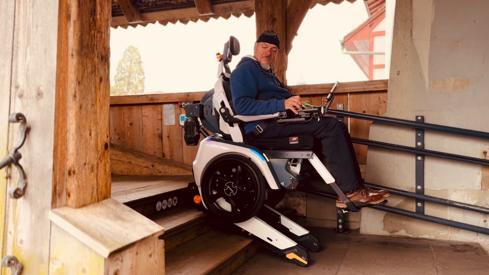 Stefan Baumgartner fährt mit seinem treppensteigenden Elektrorollstuhl Scewo BRO sicher eine Holztreppe hinauf und demonstriert den Treppenmodus.