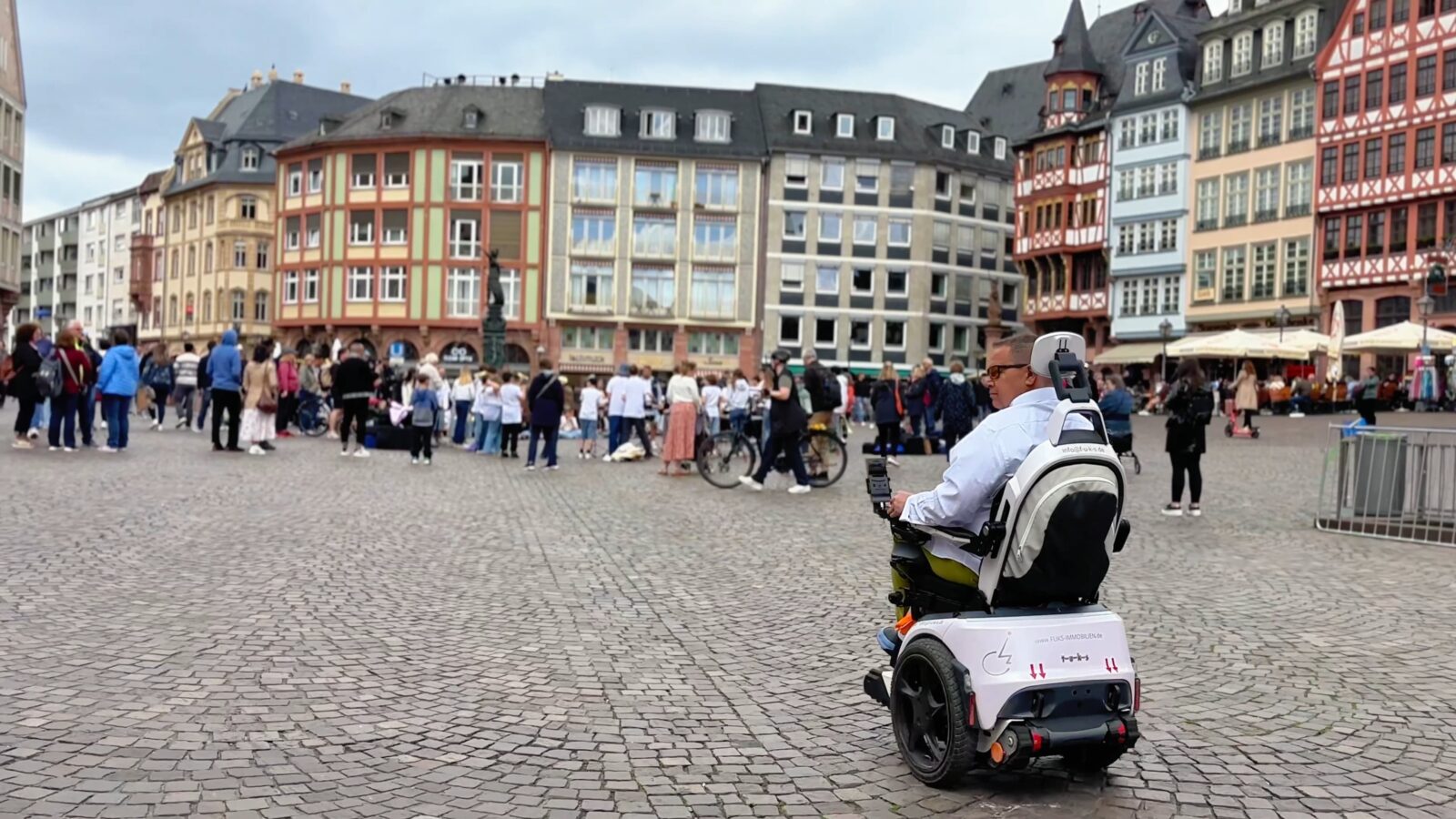 Daniel Fuks fährt mit treppensteigendem Elektrorollstuhl Scewo BRO durch Frankfurter Innenstadt mit großer Menschenmenge im Hintergrund