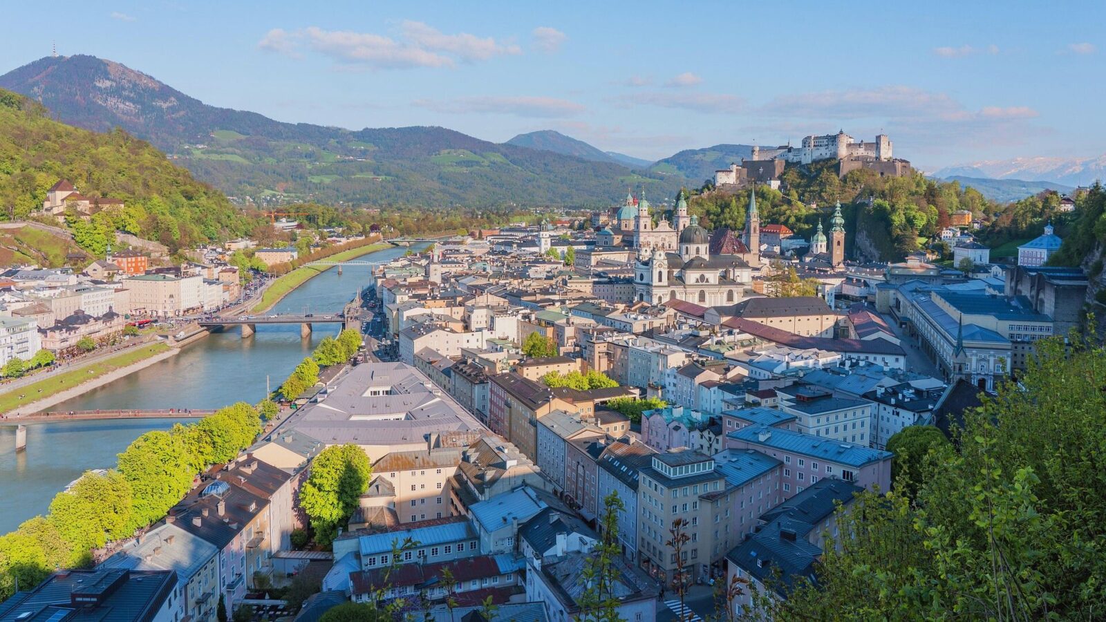 Blick über die Stadt Salzburg mit Salzach, historischen Gebäuden und umliegenden Bergen.