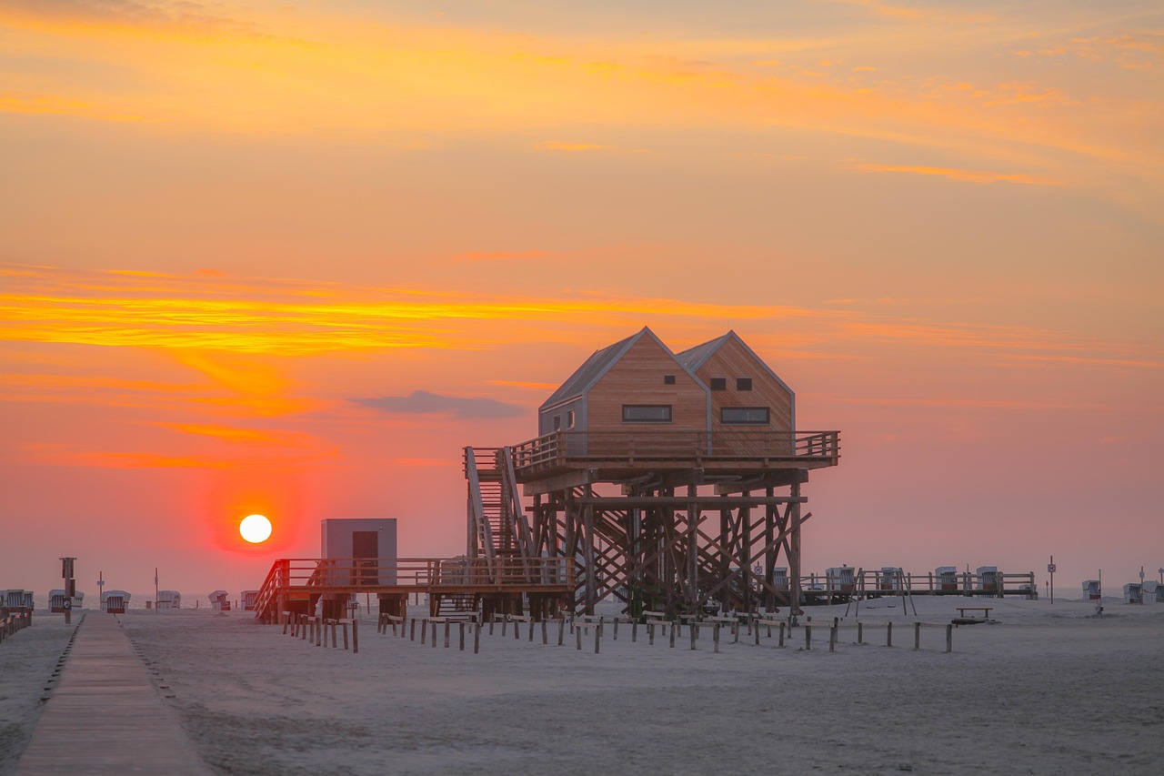 Sonnenuntergang am Strand mit Pfahlbauhäusern und orangefarbenem Himmel.