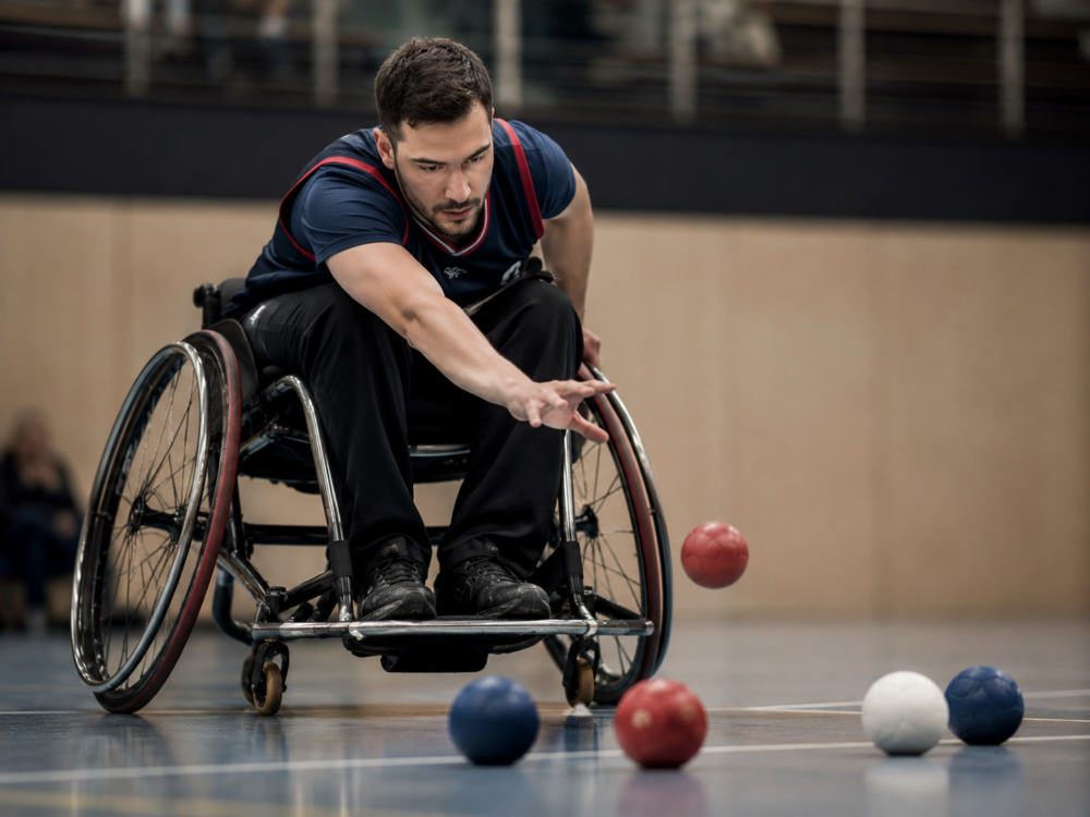 Teams aus Rollstuhlfahrern spielen Boccia in einer Sporthalle