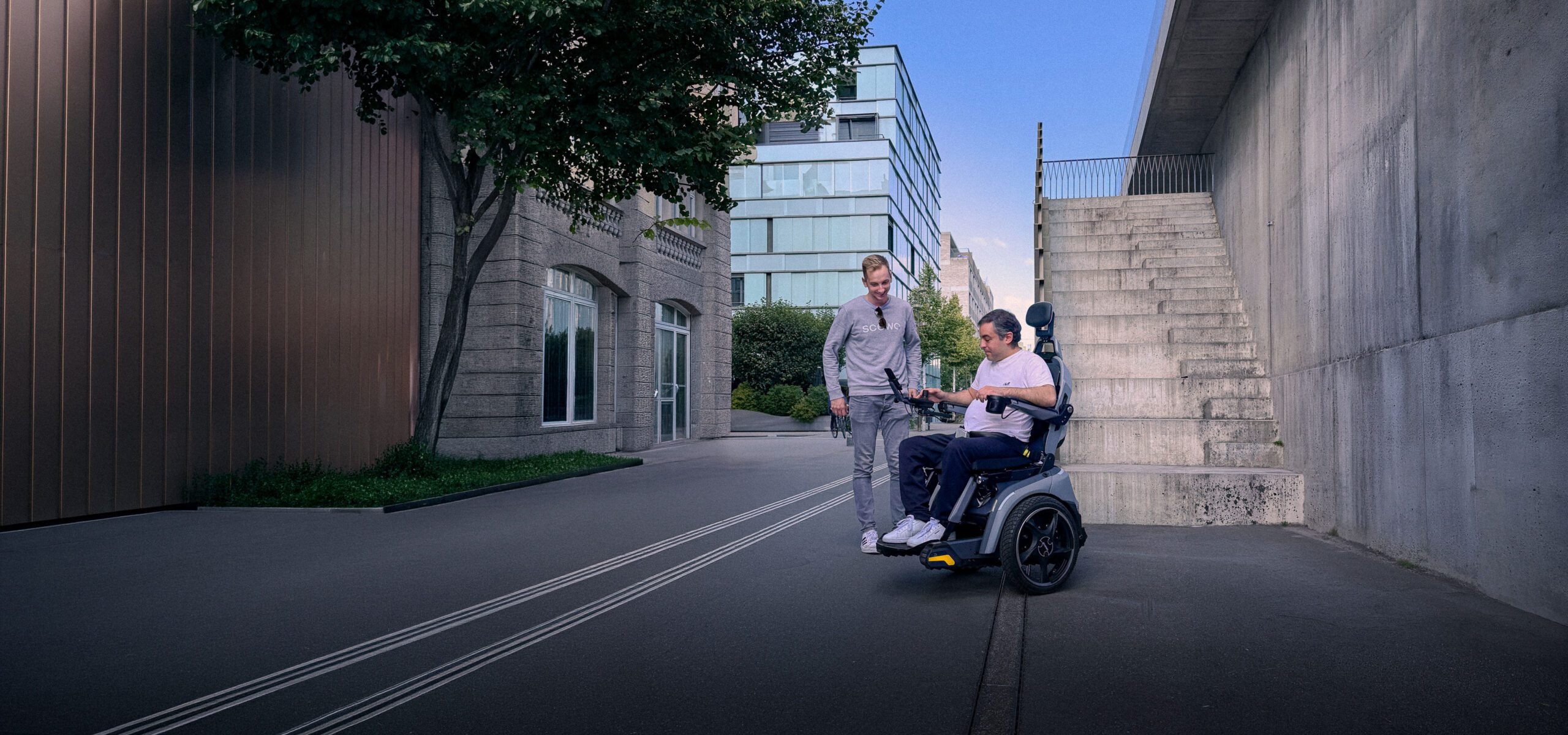 Scewo-Mitarbeiter begleitet Mann im BRO Elektrorollstuhl bei Probefahrt vor einer Aussentreppe.