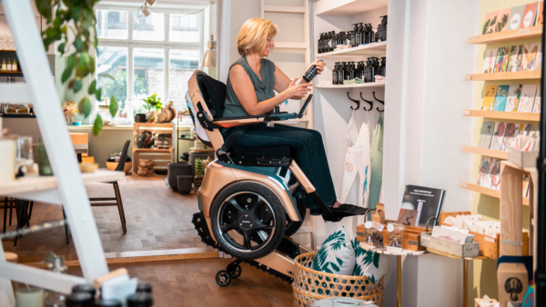 Frau im Scewo BRO nutzt den Sitzlift, um im Laden ein Regal oben zu erreichen.