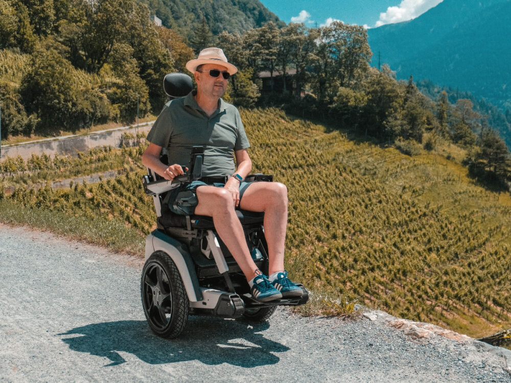 Mann im Scewo BRO Elektrorollstuhl geniesst die Aussicht auf Weinberge und Berge.