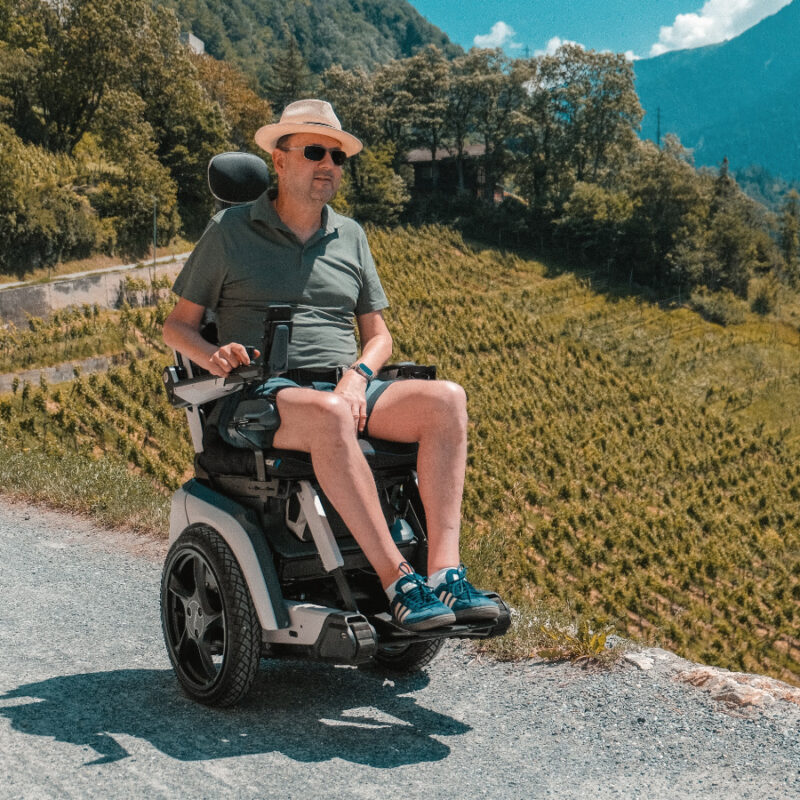 Mann im Scewo BRO Elektrorollstuhl geniesst die Aussicht auf Weinberge und Berge.