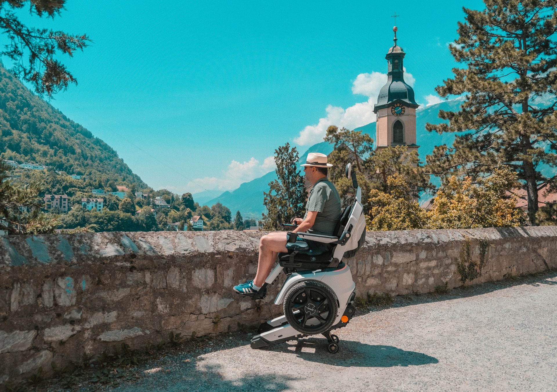 Mann im Scewo BRO mit aktivierter Höhenverstellung, Blick auf Kirchturm und Berge.