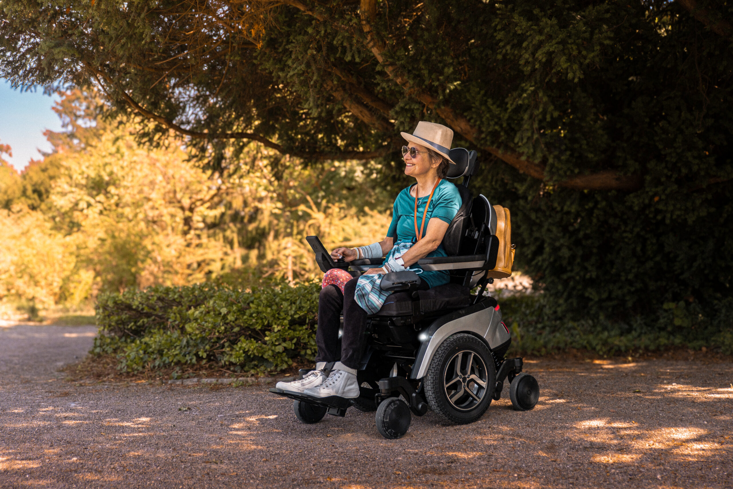 Lächelnde Frau fährt im Scewo GO Elektrorollstuhl durch einen sonnigen Park.
