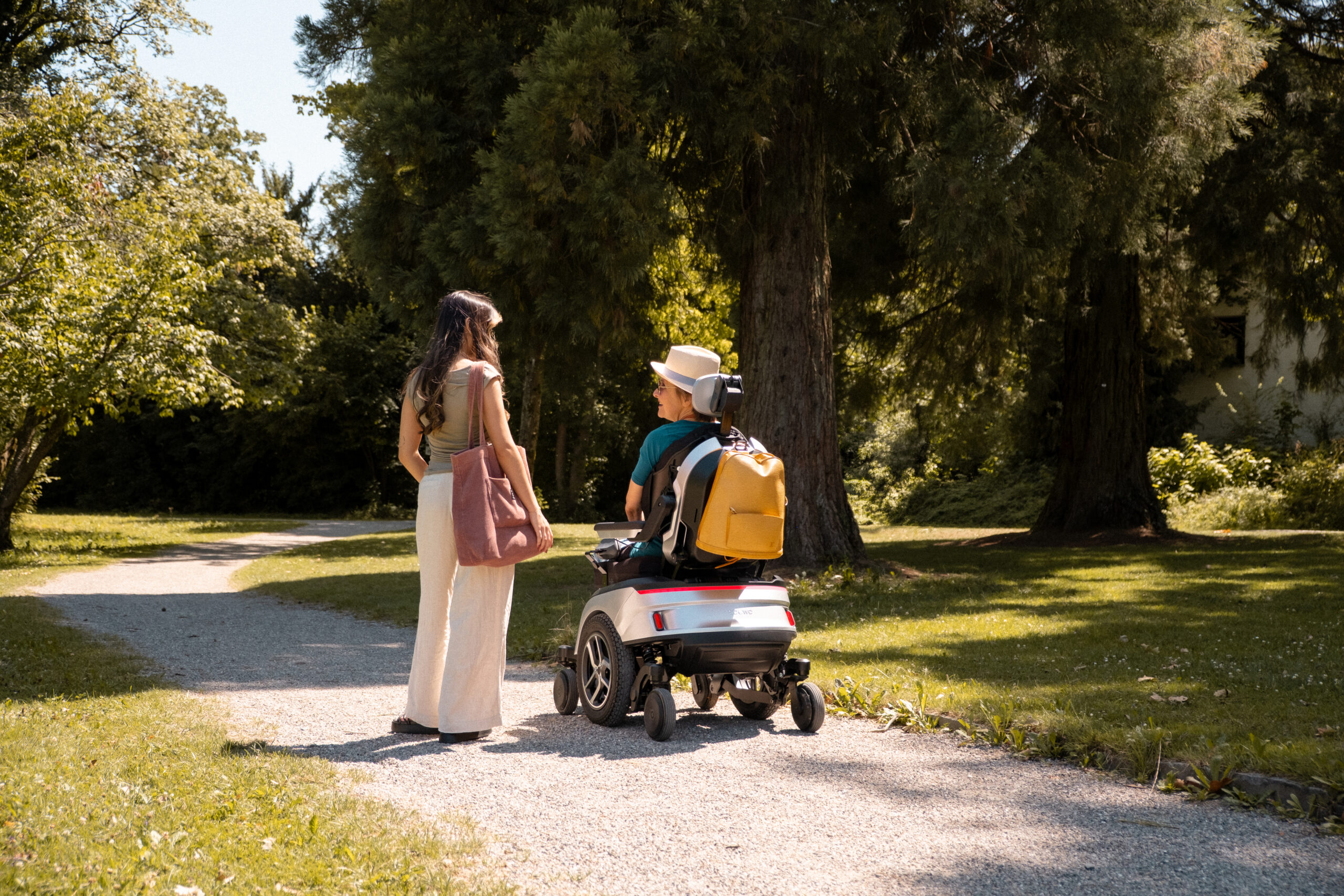 Zwei Frauen unterhalten sich auf einem Kiesweg im Park, eine sitzt im Scewo GO.
